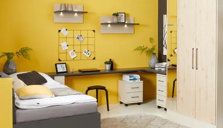 Farbenfrohes Jugendzimmer mit gelber Wand, Bett und langem Schreibtisch.